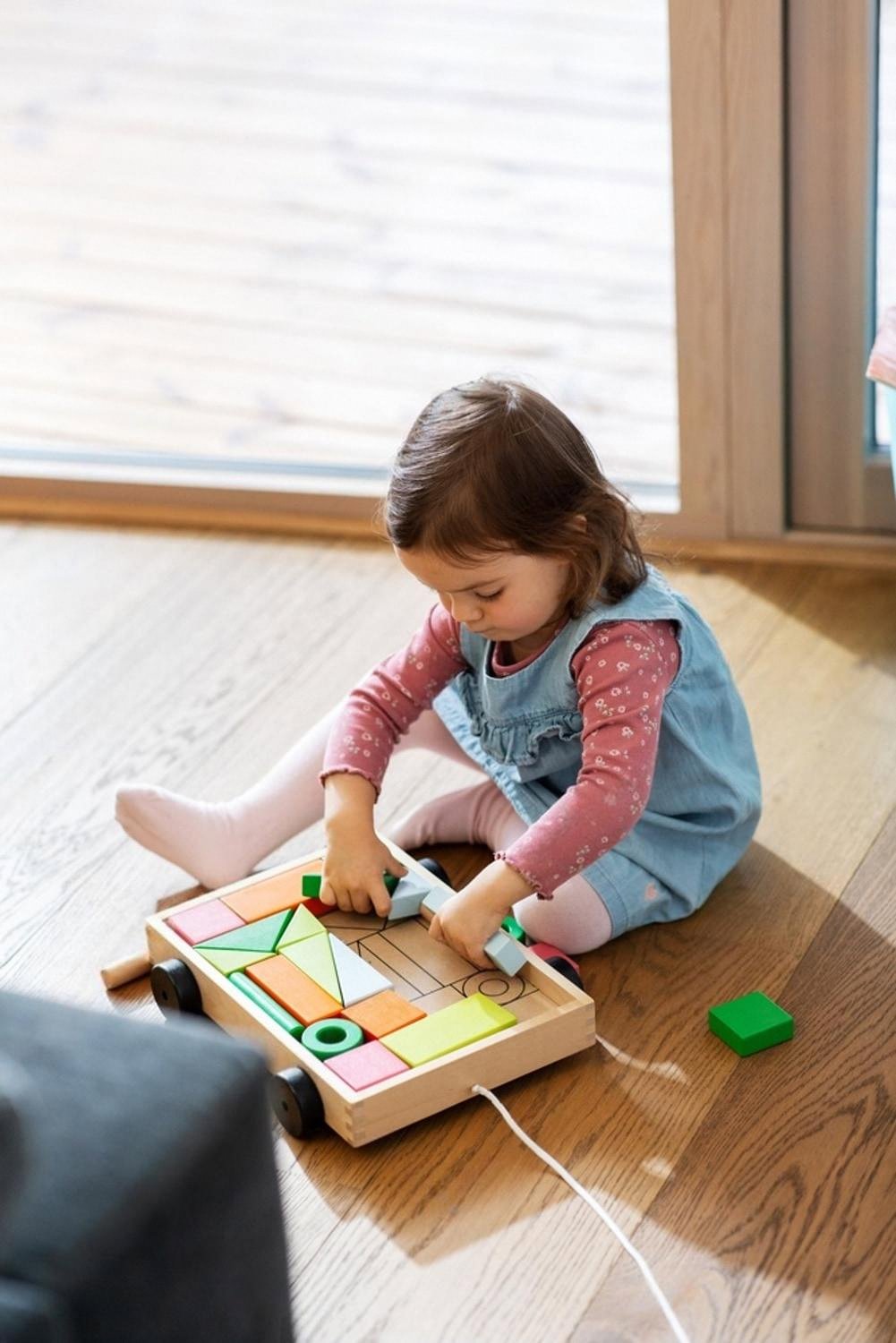 Little girl in a Dubai home playing with a wooden pull-along cart filled with sustainable blocks